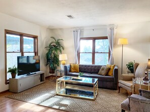 A living room with a sofa, a coffee table, a TV, and a lamp. - Stylish Apartment in Historic Downtown Parkville (Parkville)