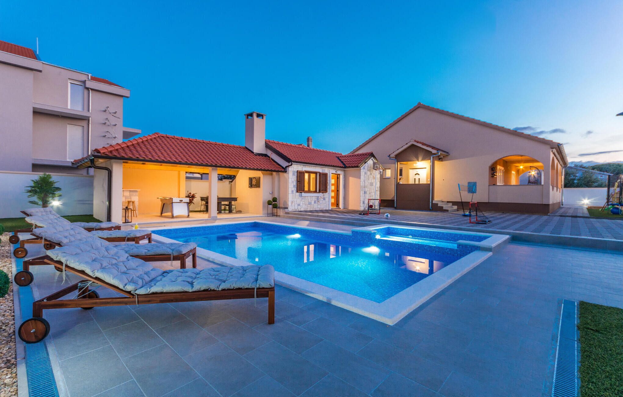 Una casa moderna con piscina, sillas de descanso y un patio bien iluminado.