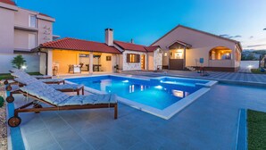 Ett modernt hus med en swimmingpool, solstolar och en väl upplyst uteplats.