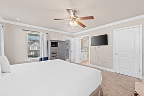 Cozy retreat with a large bed, ceiling fan, and TV, plus a door to a bathroom.