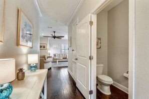 Enter a hallway leading to a bathroom and living area, featuring a sofa and coffee table.