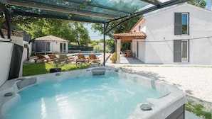A hot tub with a patio area, outdoor furniture, and a house with a white exterior and tiled roof. - Pet friendly home in Krnicari (Krnicari)