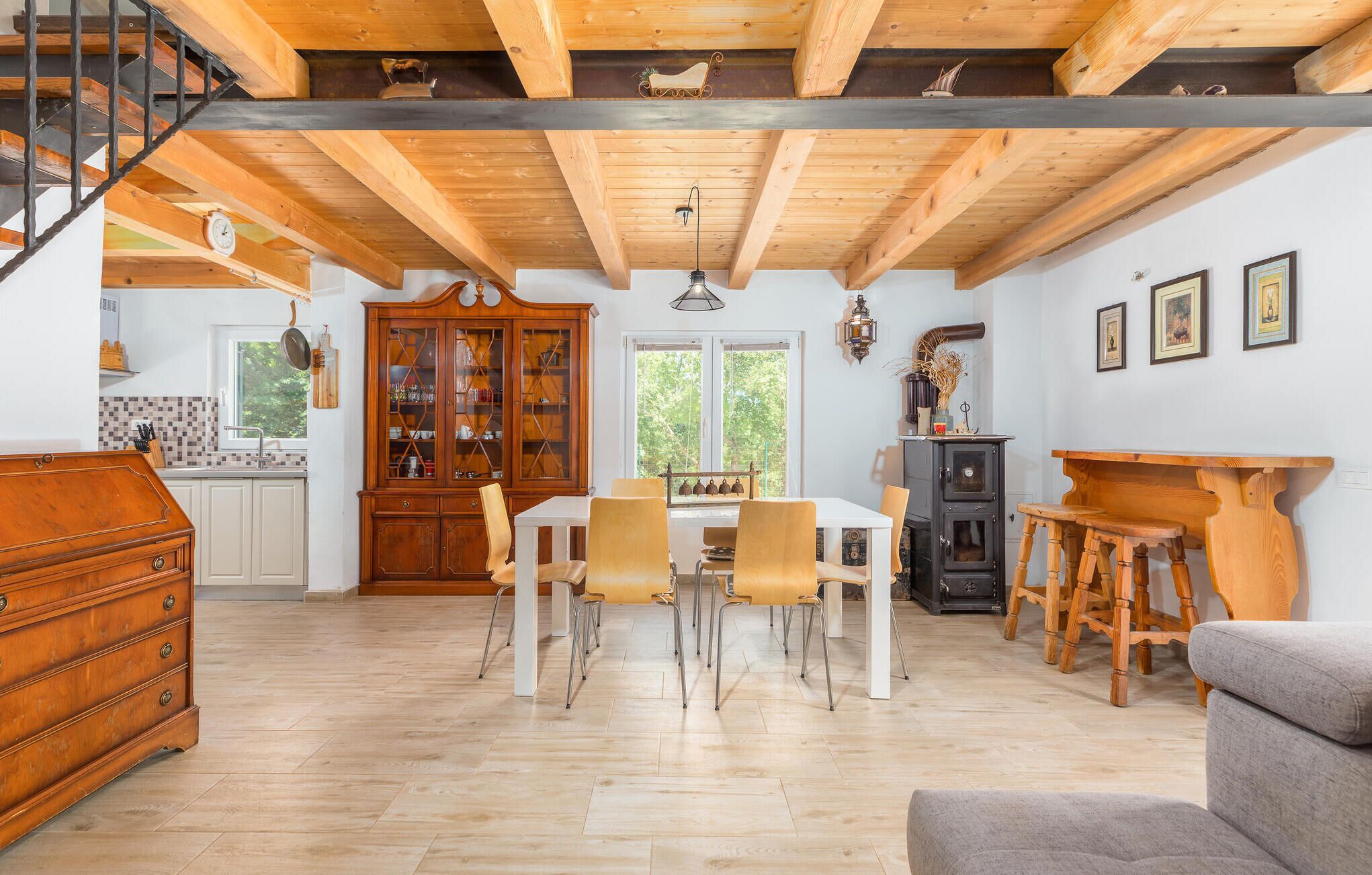 A spacious kitchen with wooden cabinets, a dining area with a white table and chairs, and a staircase with a metal railing.