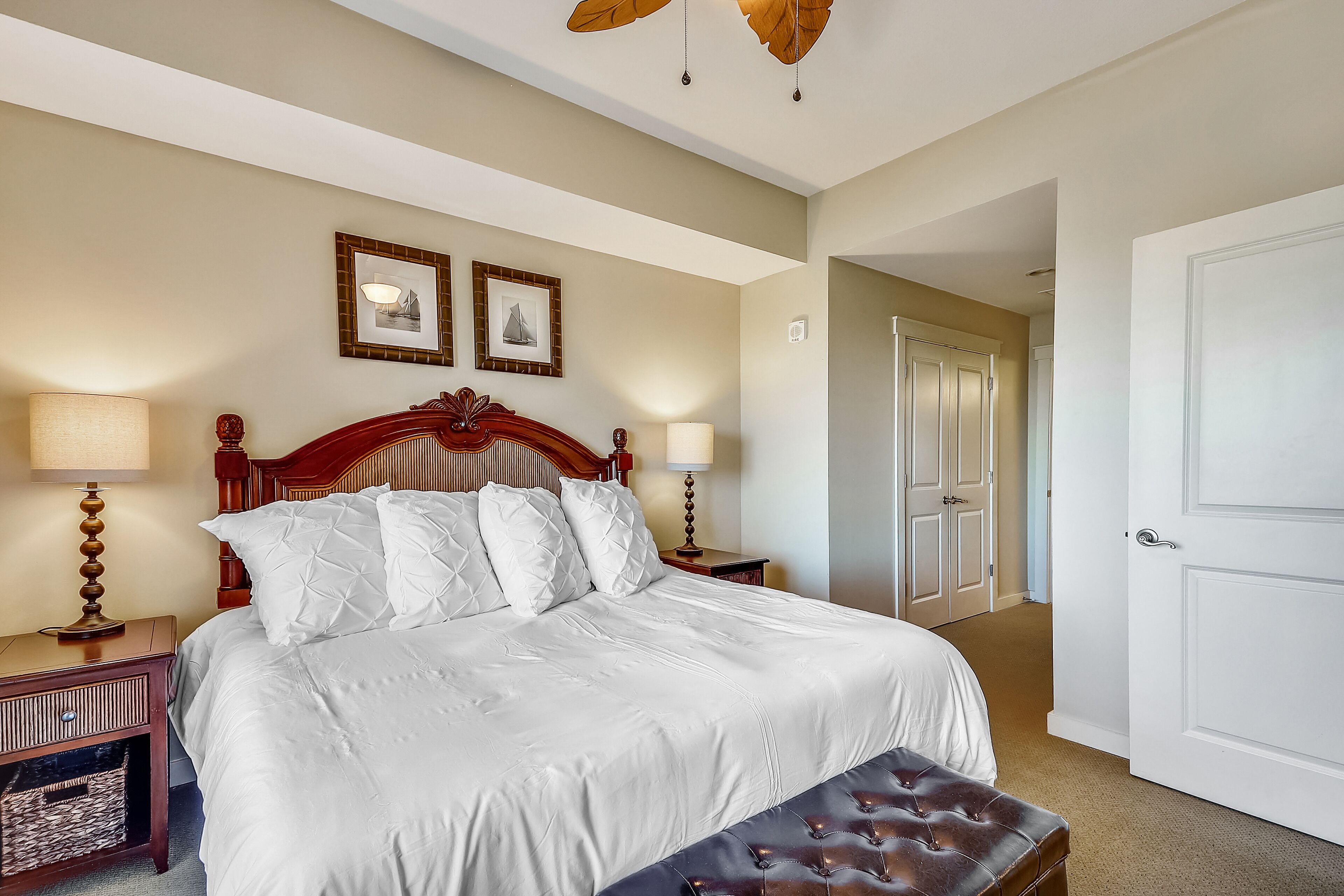 A neatly made bed with white linens, a wooden headboard, and two bedside lamps.