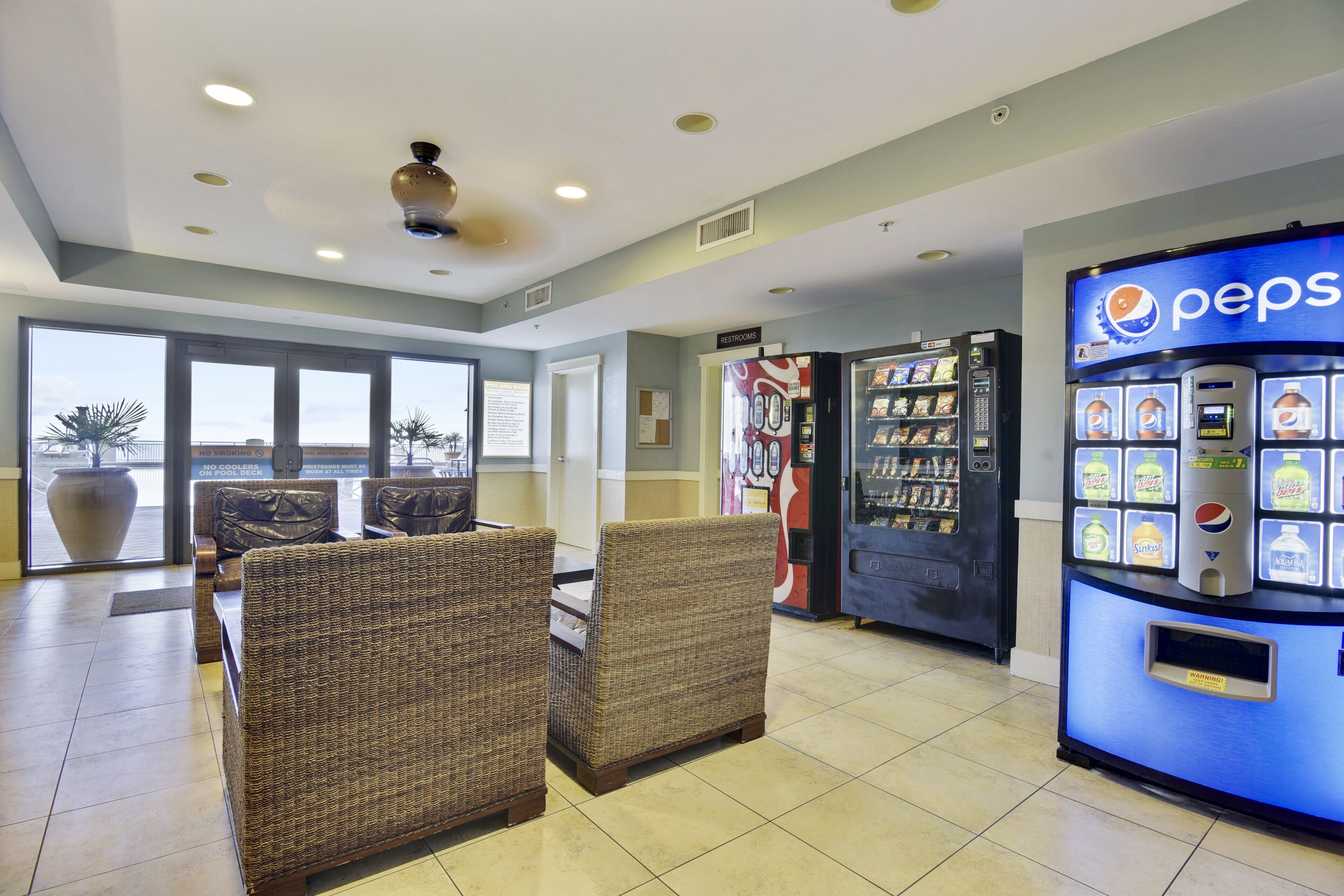 A lobby with wicker chairs, a Pepsi vending machine, and a large window with a view.