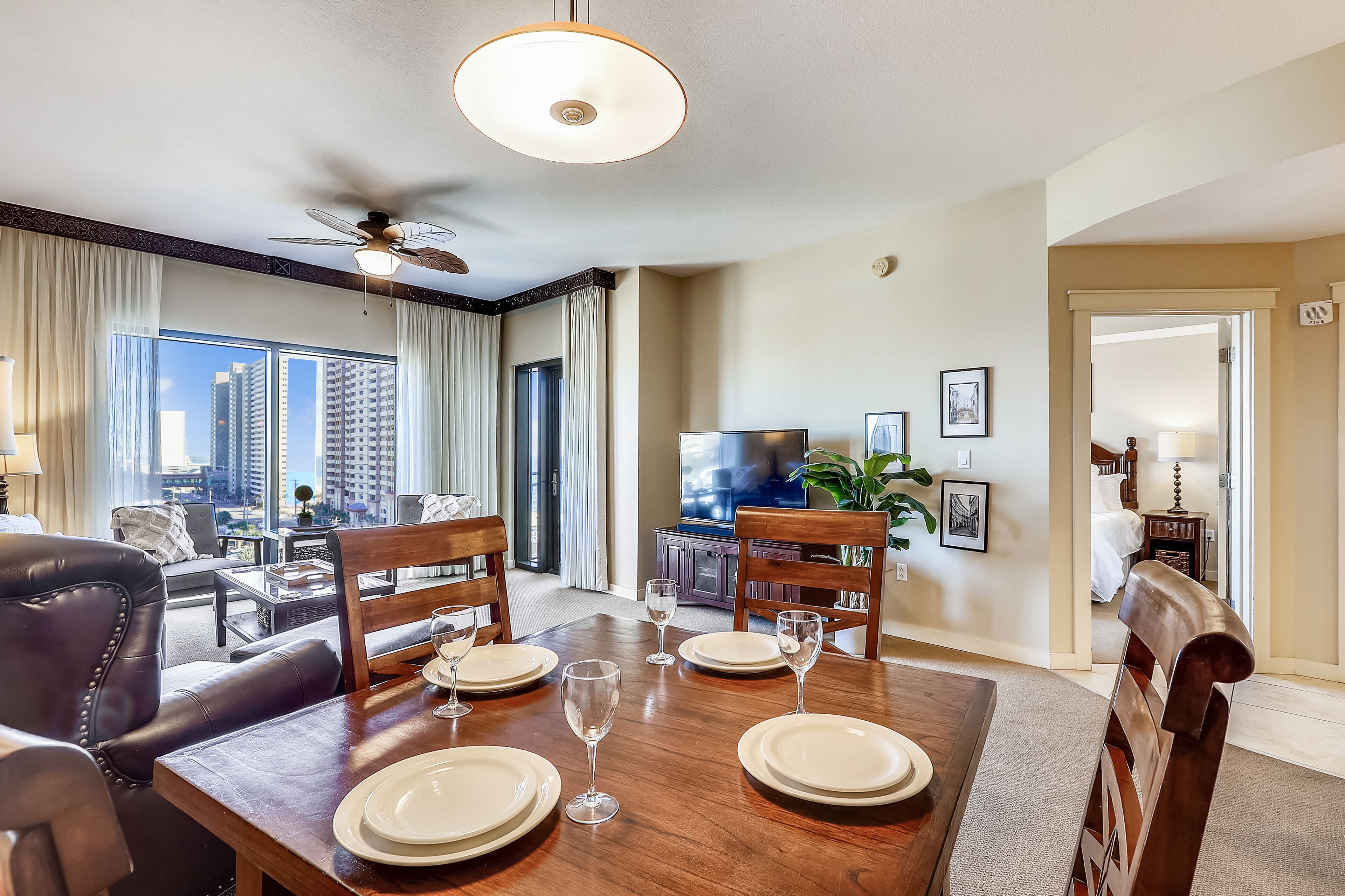 A dining area with a table set for four, a ceiling fan, and a city view through large windows.