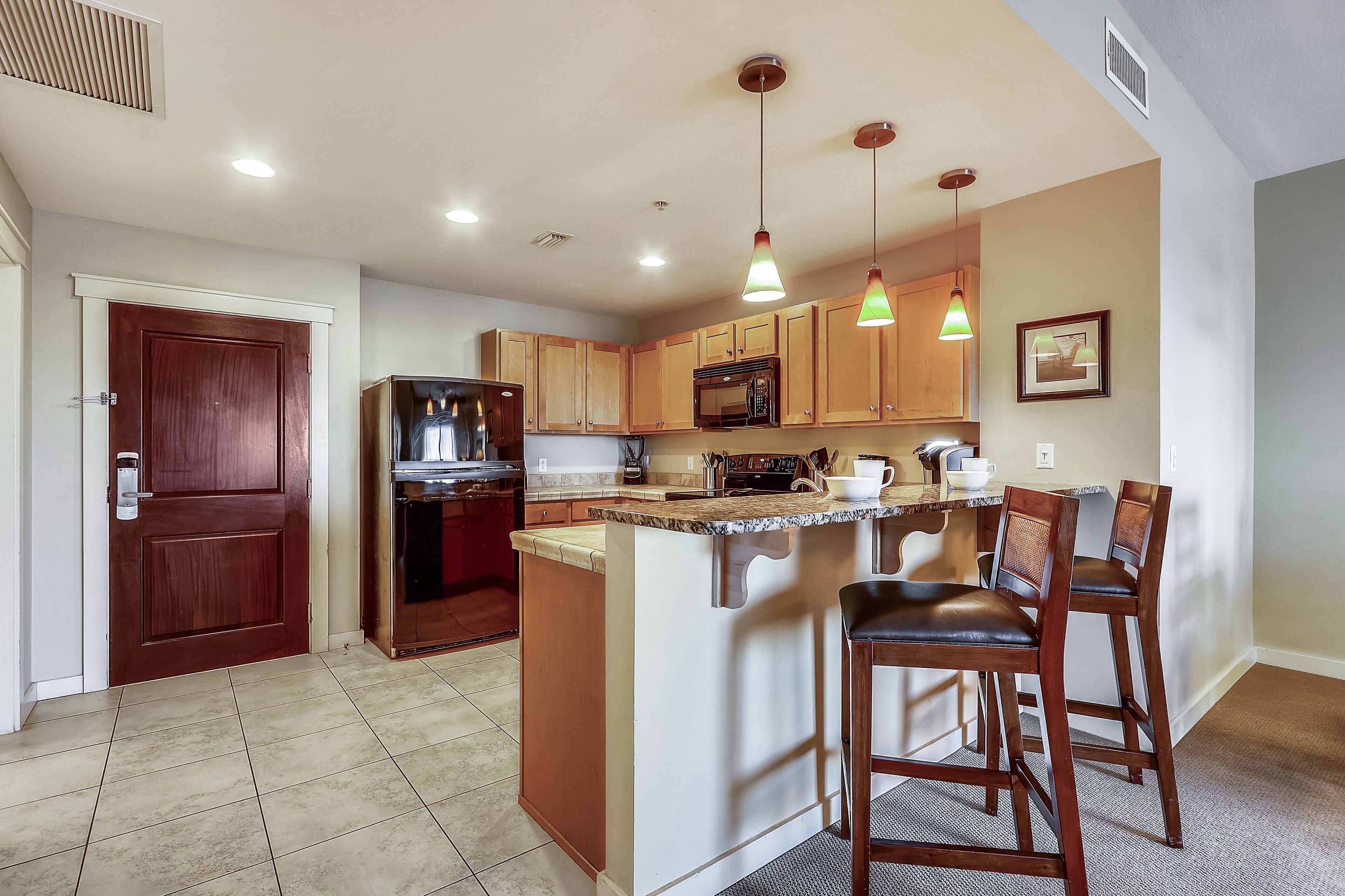 A modern kitchen with wooden cabinets, a built-in microwave, and a central island with bar stools.