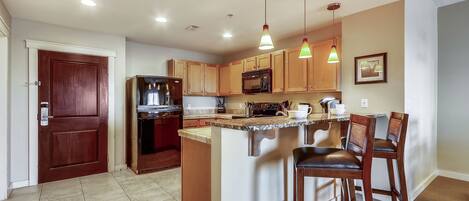 A modern kitchen with wooden cabinets, a built-in microwave, and a central island with bar stools.