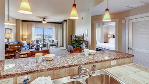 Habitación de hotel con cocina, sala de estar con sofá y sillones, comedor y dormitorio con cama y cortinas.
