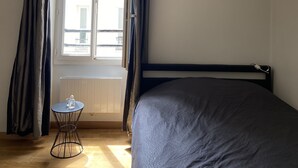 A bedroom with a bed, a window with curtains, a radiator, and a small round table with a glass object on it. - Studio ideally located and quiet 15 eme arrondissement (Paris)