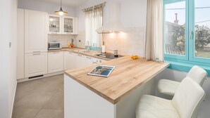 Een moderne keuken met witte kasten, een houten aanrecht, een inbouwoven en een raam met uitzicht.