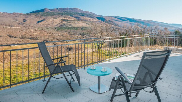 Een terras met twee stoelen en een tafel, met uitzicht op een bergachtig landschap.