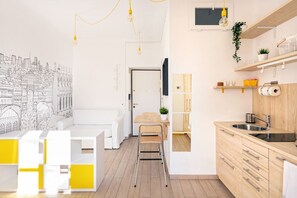 A modern kitchen with wooden cabinets, a sink, and a dining area with a white table and yellow accents.