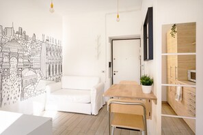 Un salon moderne avec un canapé blanc, une table à manger en bois et une fresque représentant un paysage urbain sur le mur.