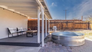 Ein überdachter Patio-Bereich mit Gartenmöbeln, einem Whirlpool und einem Holzzaun im Hintergrund.