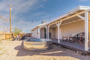 A covered outdoor patio with a hot tub, seating area, and a wooden fence.
