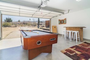 A pool table with a dartboard and stools in a room with a view through a glass door. - JT Agave Oasis | 3BR + Game Room + Cowboy Pool (Joshua Tree)