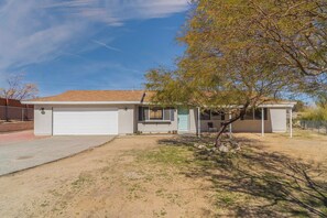 A single-story house with a garage, a covered patio, and a tree in the yard. - JT Agave Oasis | 3BR + Game Room + Cowboy Pool (Joshua Tree)