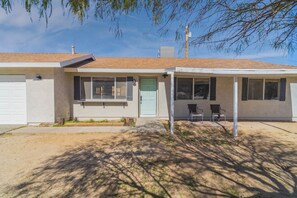 A single-story house with a front porch, a garage door, and a small front yard with two chairs. - JT Agave Oasis | 3BR + Game Room + Cowboy Pool (Joshua Tree)