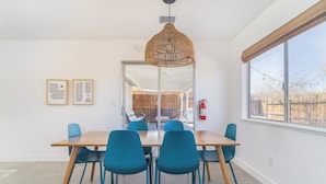 Un comedor moderno con una mesa de madera y sillas color turquesa, una lámpara colgante tejida y un ventanal con vistas al exterior.
