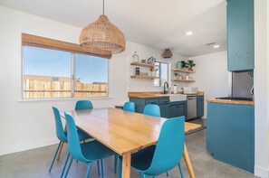 A modern kitchen with a wooden dining table and blue chairs, a hanging light fixture, and built-in cabinets.