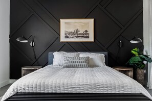 Une chambre à coucher avec un lit, deux lampes de chevet, un tableau encadré au mur et une plante en pot.