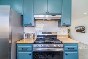 A kitchen with teal cabinets, a stainless steel refrigerator, a double toaster, a gas stove, and an oven. - JT Agave Oasis | 3BR + Game Room + Cowboy Pool (Joshua Tree)