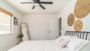 Un dormitorio con cama, ventilador de techo, espejo y decoración en las paredes.
