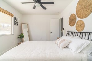 A bedroom with a bed, a ceiling fan, a mirror, and wall art. - JT Agave Oasis | 3BR + Game Room + Cowboy Pool (Joshua Tree)