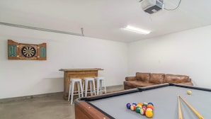 Ein Billardtisch mit Kugeln, ein braunes Ledersofa und eine Dartscheibe.