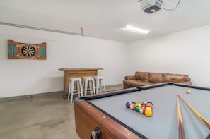 Une table de billard avec des billes, un canapé en cuir marron et un jeu de fléchettes.