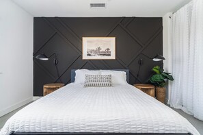 A bedroom with a bed, two bedside tables, a wall-mounted picture, and a potted plant.