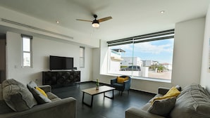 A modern living room with a flat-screen TV, a ceiling fan, and large windows offering a city view. - Welcome to Your Perfect Beach Getaway F19, Welcome to Your Perfect Beach Getaway F19 (puerto penasco)