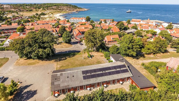 Vue aérienne d’une ville côtière avec des maisons aux toits rouges, une marina et un grand bâtiment doté de panneaux solaires.
