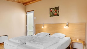 Une chambre à coucher avec une tête de lit en bois, un lit recouvert de linge de lit blanc, une petite table de chevet avec une bougie et une fenêtre à vitres dépolies.