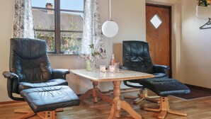 Une pièce comprenant deux fauteuils en cuir noir, une table en bois et une fenêtre ornée de rideaux à motifs floraux.