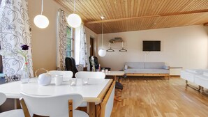 Un salon moderne avec un plafond en bois, un canapé, un téléviseur et un coin repas comprenant une table et des chaises.