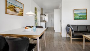 Ein modernes, helles Wohnzimmer mit Essbereich, ausgestattet mit einem Holztisch, schwarzen Ledersesseln, einer schwarzen Ledercouch und zwei Bildern an den Wänden.