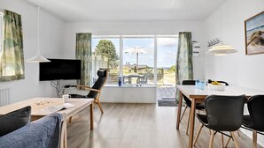 Ein modernes Wohnzimmer mit Fernseher, Sitzgelegenheiten und Blick ins Freie.