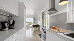 Eine moderne Küche mit weißen Schränken, einem großen Fenster und Blick ins Freie.