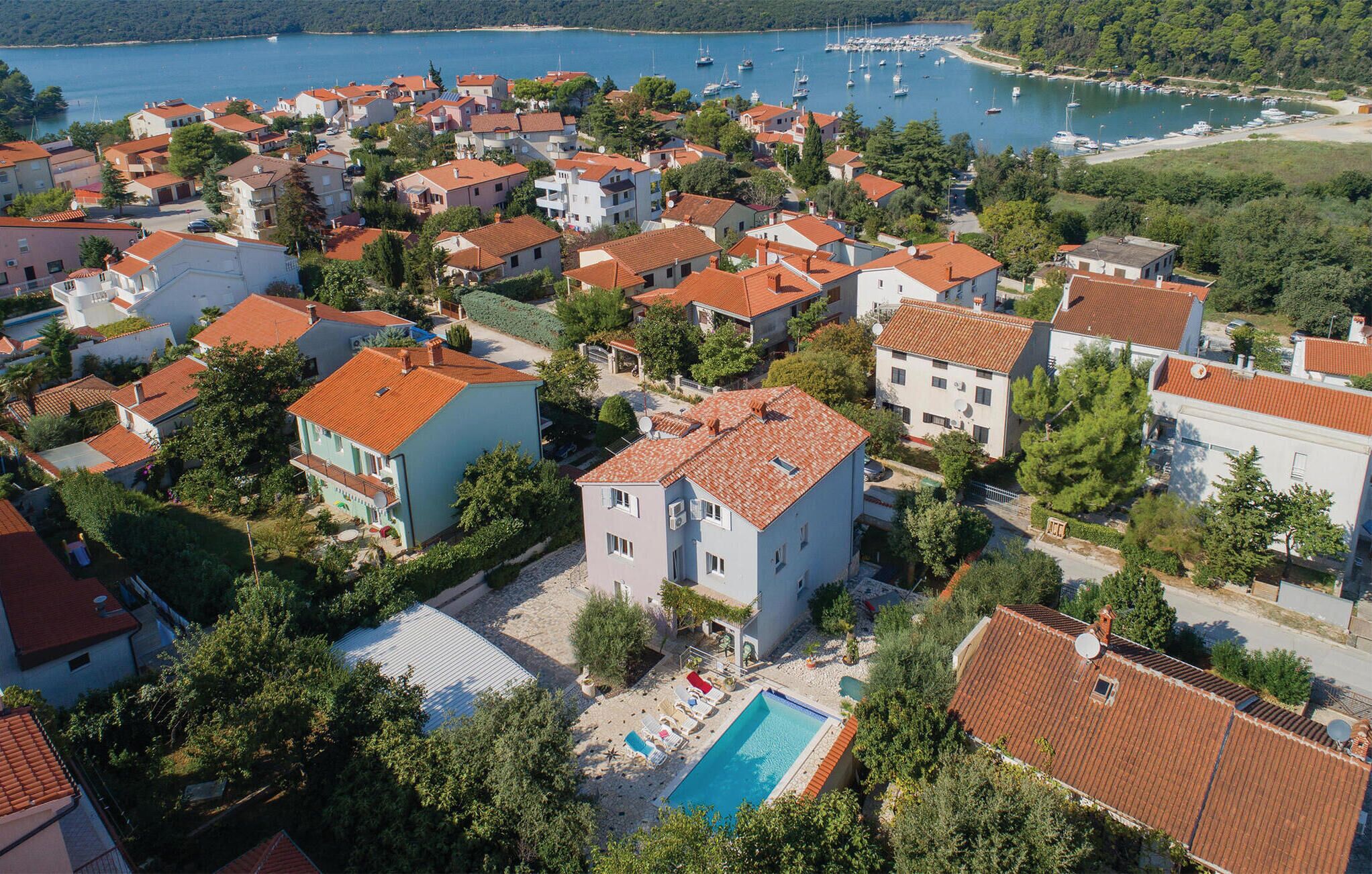 An aerial view of a coastal residential area with houses, a swimming pool, and a marina with boats.