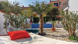 Eine Hängematte mit rotem Kissen, ein kleiner Pool und Kübelpflanzen in einem Innenhof mit einer Kachelwand und einem Gebäude im Hintergrund.