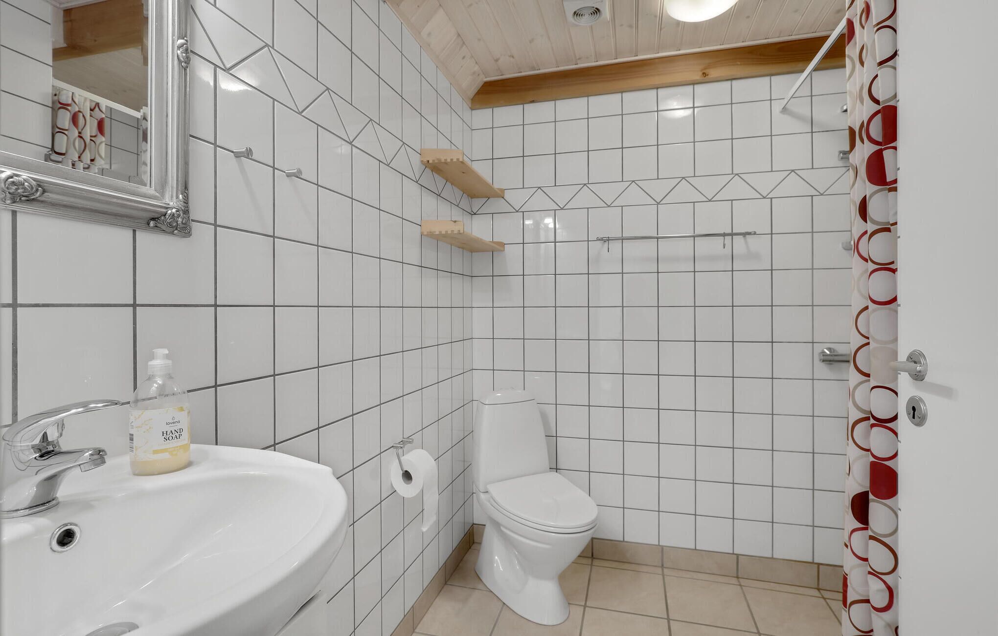 Ein Badezimmer mit weißen Fliesen, einem Waschbecken, einer Toilette und einer Duschvorhang.