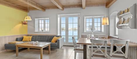 A cozy living room with a sofa, coffee table, and dining table. There are two windows with views of a snowy landscape.