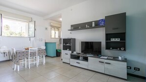 A modern living room with a TV, built-in shelves, and a dining area with a table and chairs. - Cozy apartment in Cava D'Aliga with WiFi (Cava D'Aliga)