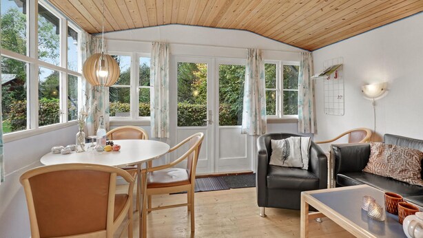 Een knus vertrek met een houten plafond, een ronde eettafel met stoelen, een zwarte leren bank en een klein bijzettafeltje.