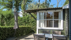 Een terras met rieten meubels, een tafel en een raam met uitzicht op een tuin.