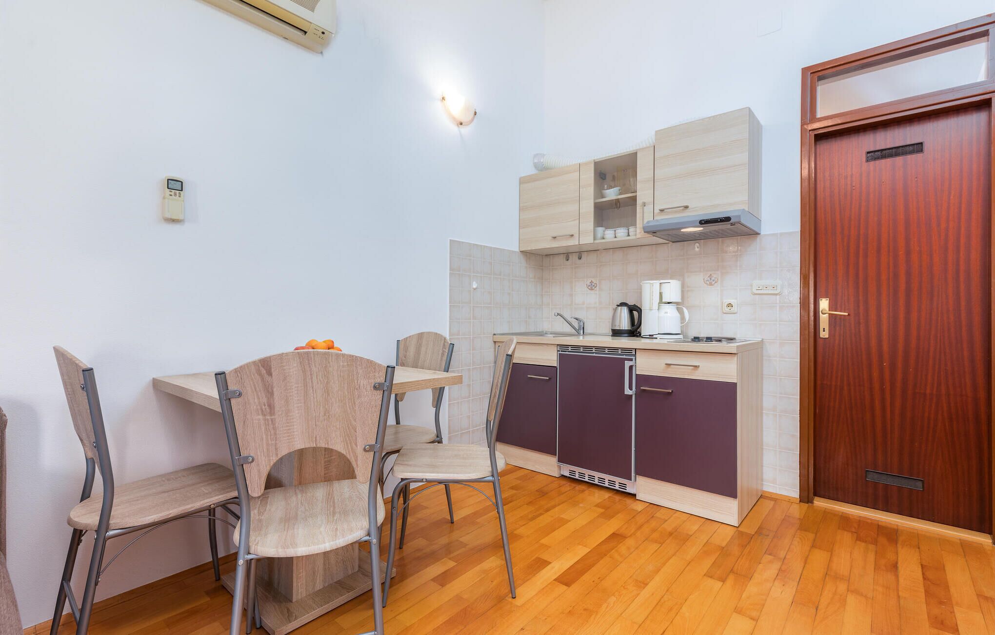 Een kleine keuken met een eettafel, stoelen, een koffiezetapparaat en een houten deur.