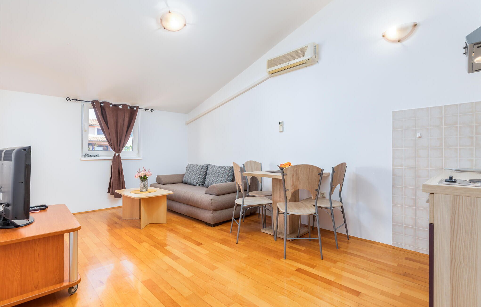 A compact living space with a sofa, dining table, chairs, a small side table, a TV, and a kitchenette area.