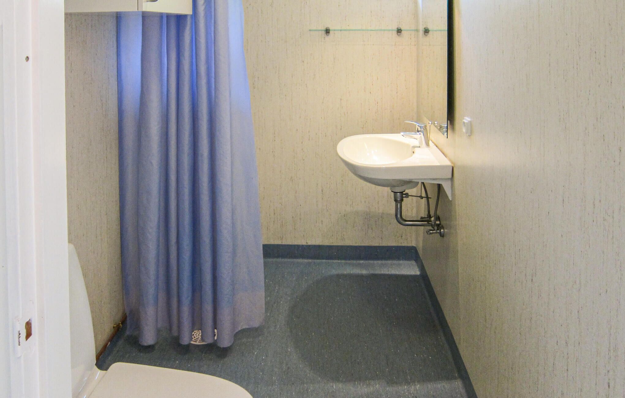 A small bathroom with a white sink, a blue shower curtain, and a tiled floor.